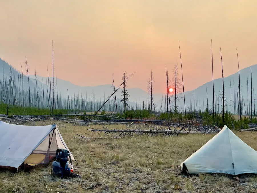 Sunset with smoke in the sky, two tents in the foreground