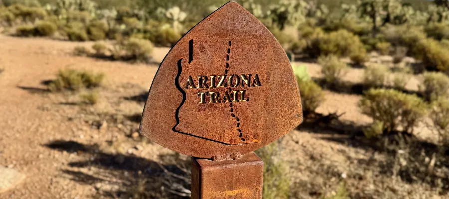 A rusting sign post with an Arizona Trail emblem on top