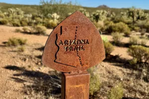 A rusting sign post with an Arizona Trail emblem on top